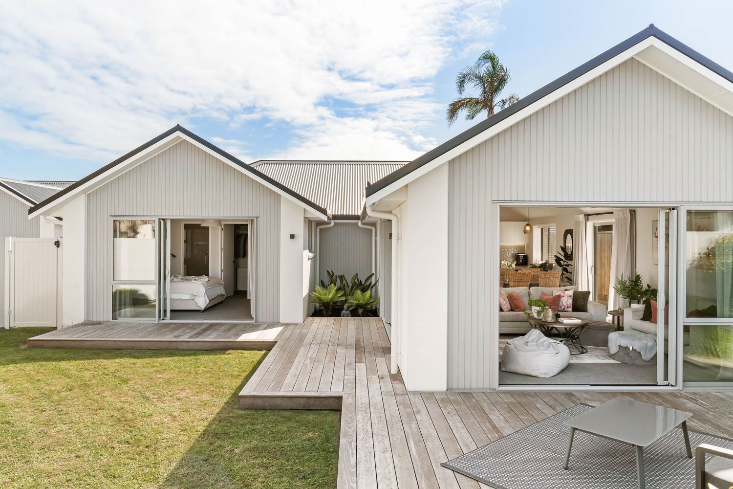 Modern coastal home with white exterior and spacious wooden deck overlooking grassy yard.