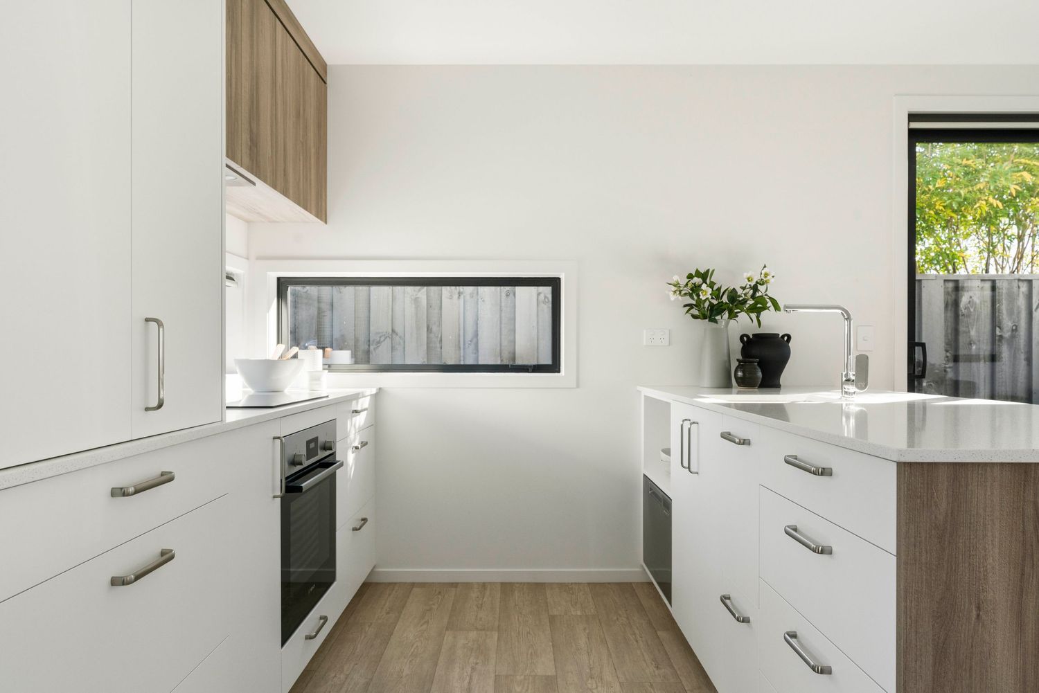 Modern white kitchen interior with wooden accents and stainless steel appliances arranged in a sleek linear design.