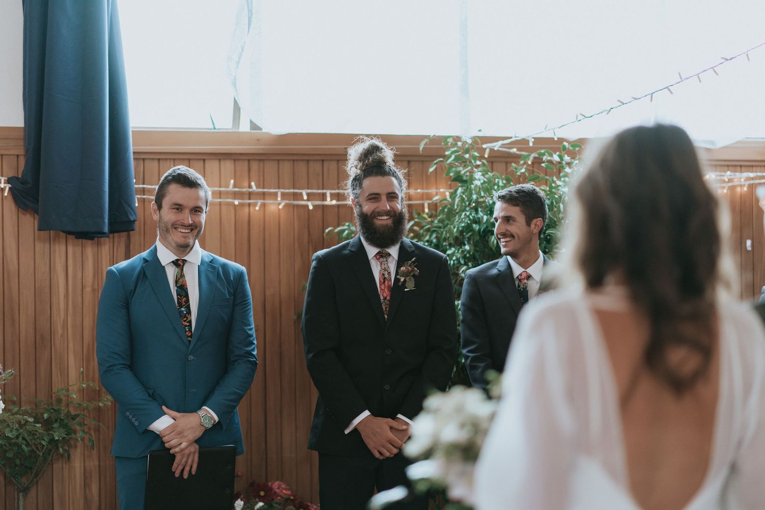 Wedding party smiles and reacts emotionally during outdoor ceremony at rustic venue with wooden fence backdrop.