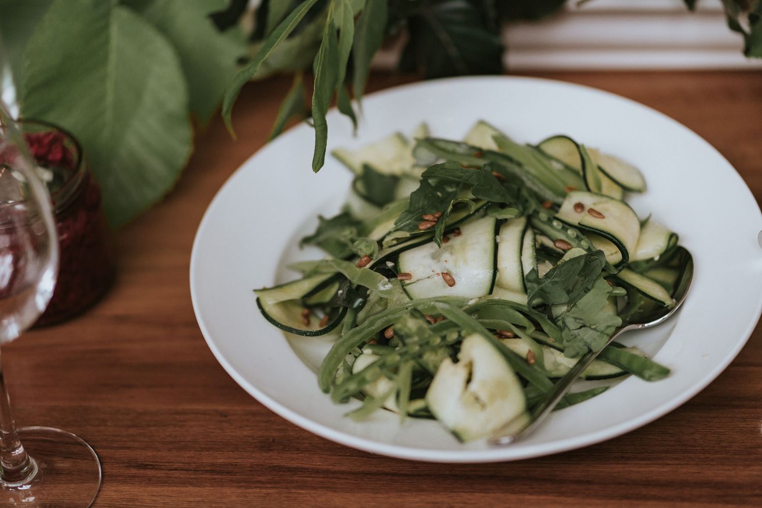 Fresh zucchini ribbons and mozzarella salad served on a white plate against a wooden table surface.