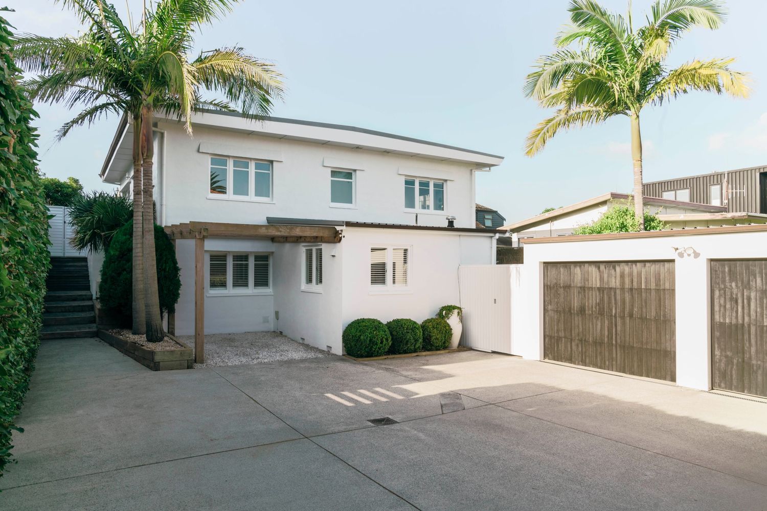 White modern house exterior with concrete driveway and palm trees in tropical setting.
