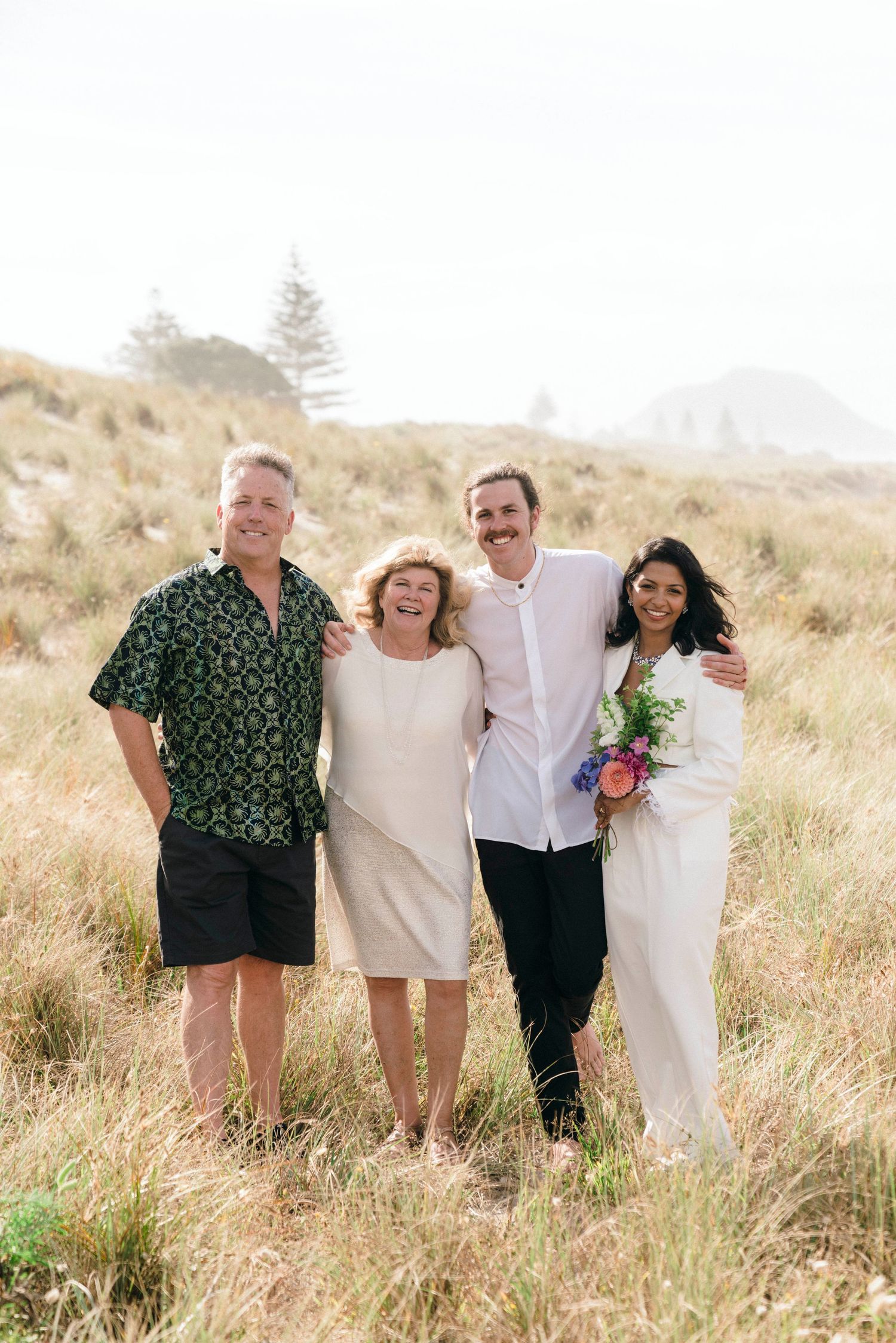 Small family group poses together on a sunny hillside during a wedding celebration.