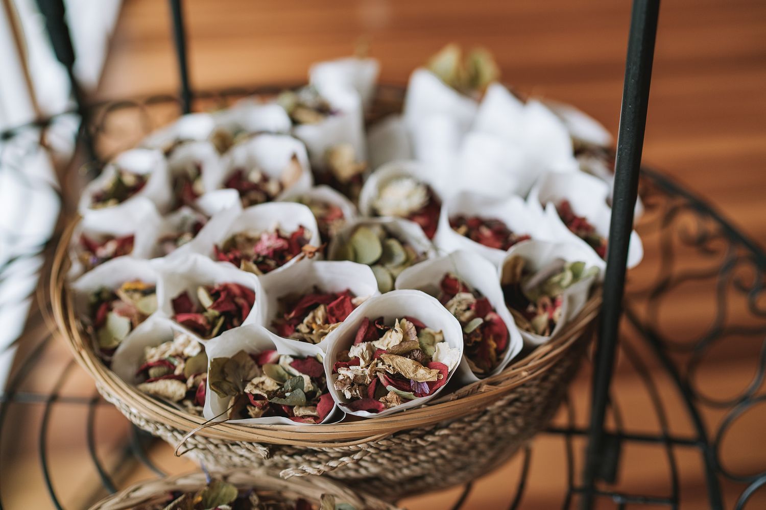 A decorative wire basket filled with wrapped dried flower petals or confetti cones made with white paper for wedding toss.