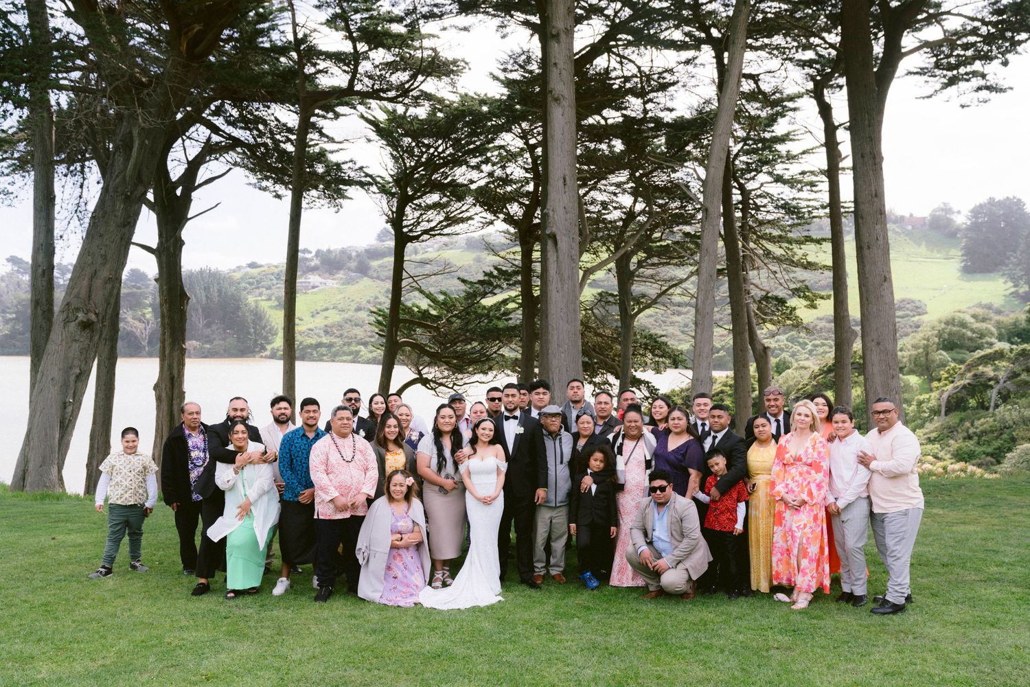 Large group photo of wedding guests gathered outdoors among tall pine trees on a misty day.