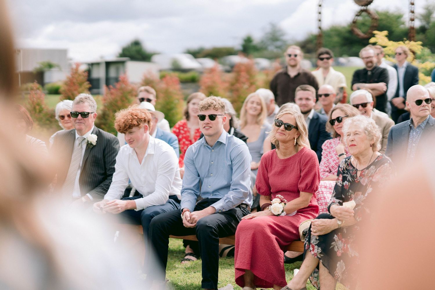 Wedding guests seated in rows on white chairs during an outdoor ceremony.