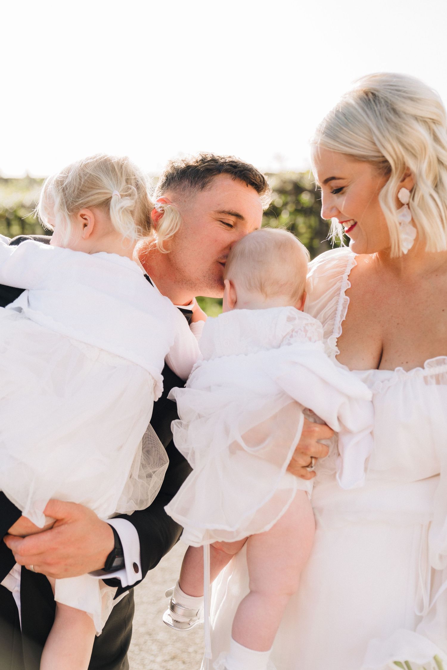 Wedding couple sharing tender moment with two children dressed in white.