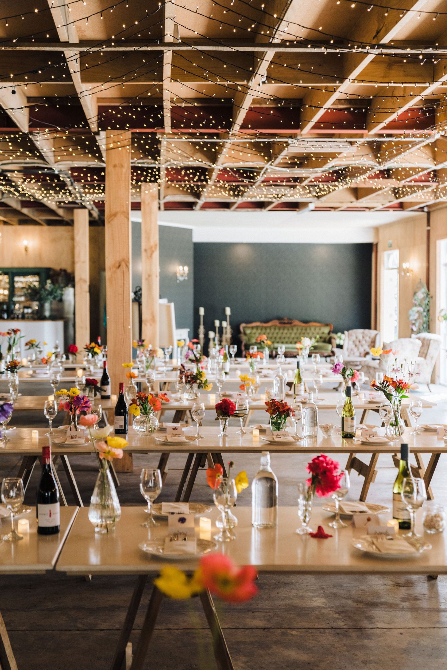 Elegant wedding reception setup with string lights, long tables and colorful floral centerpieces.