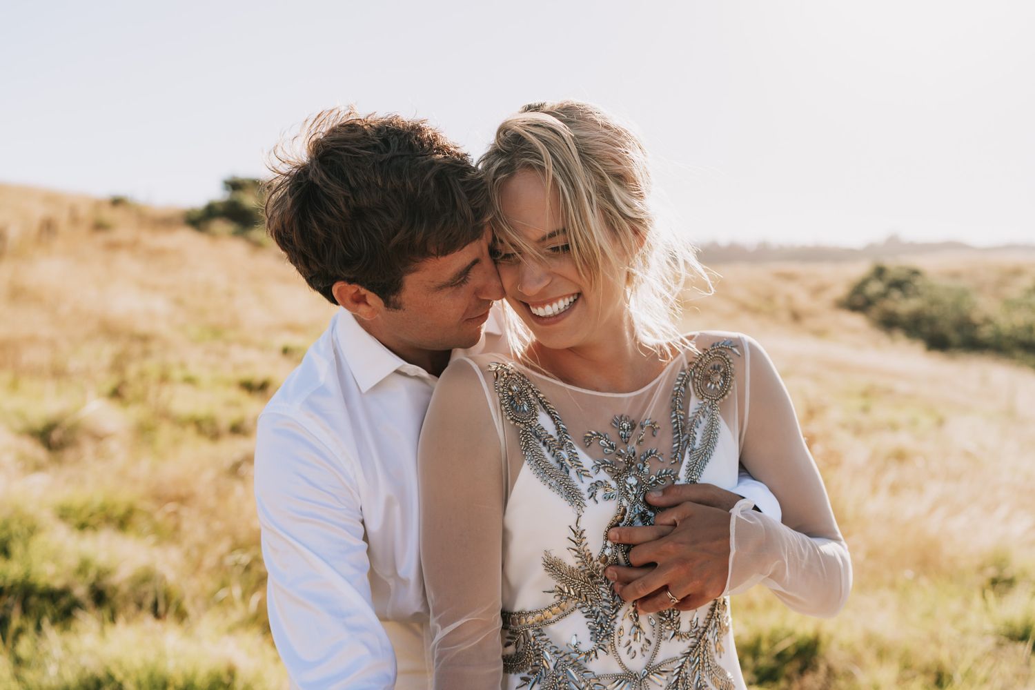 A loving couple embraces in a sun-drenched meadow during a romantic outdoor photo session.
