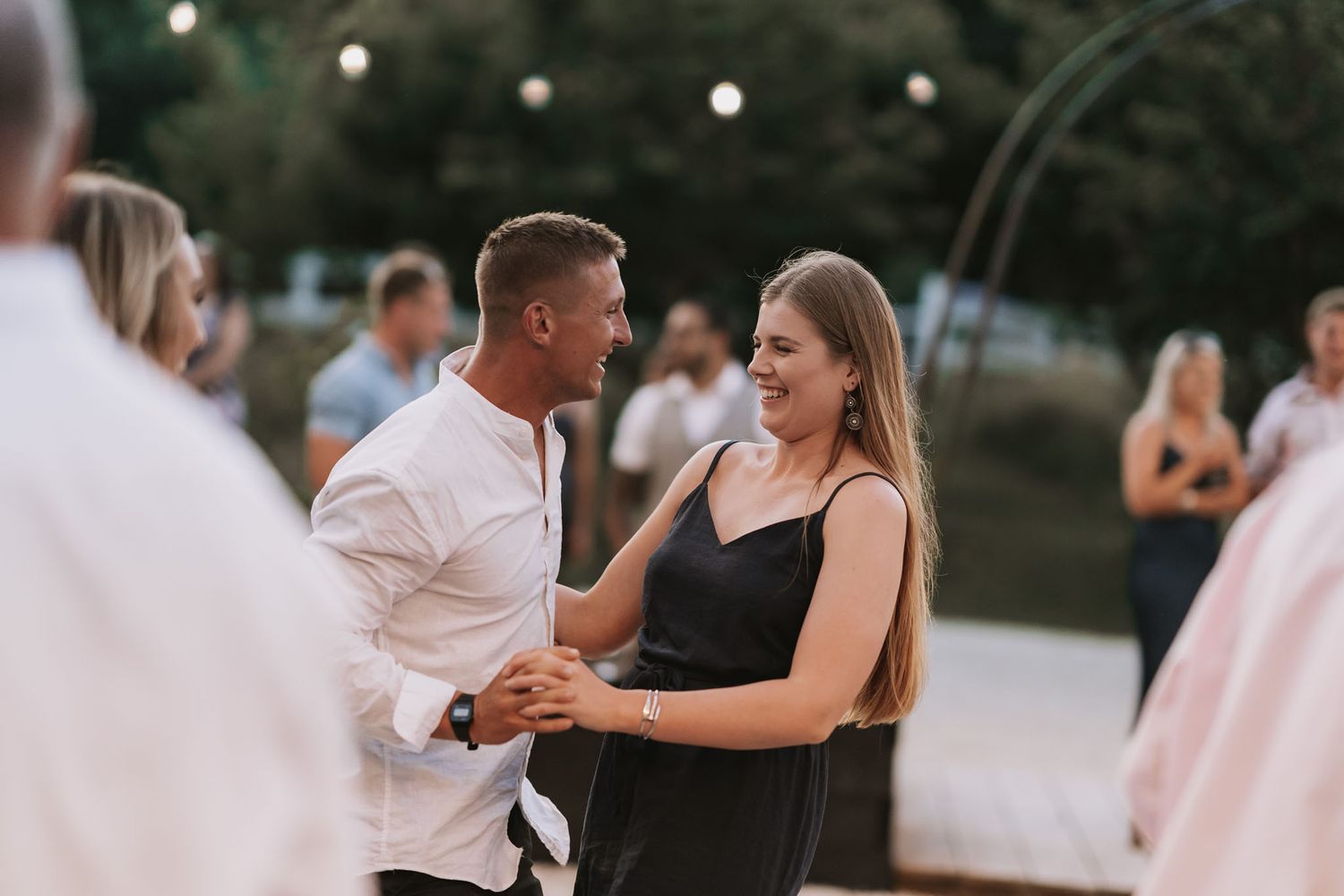 A couple dances together at an outdoor evening event with string lights visible in the background.