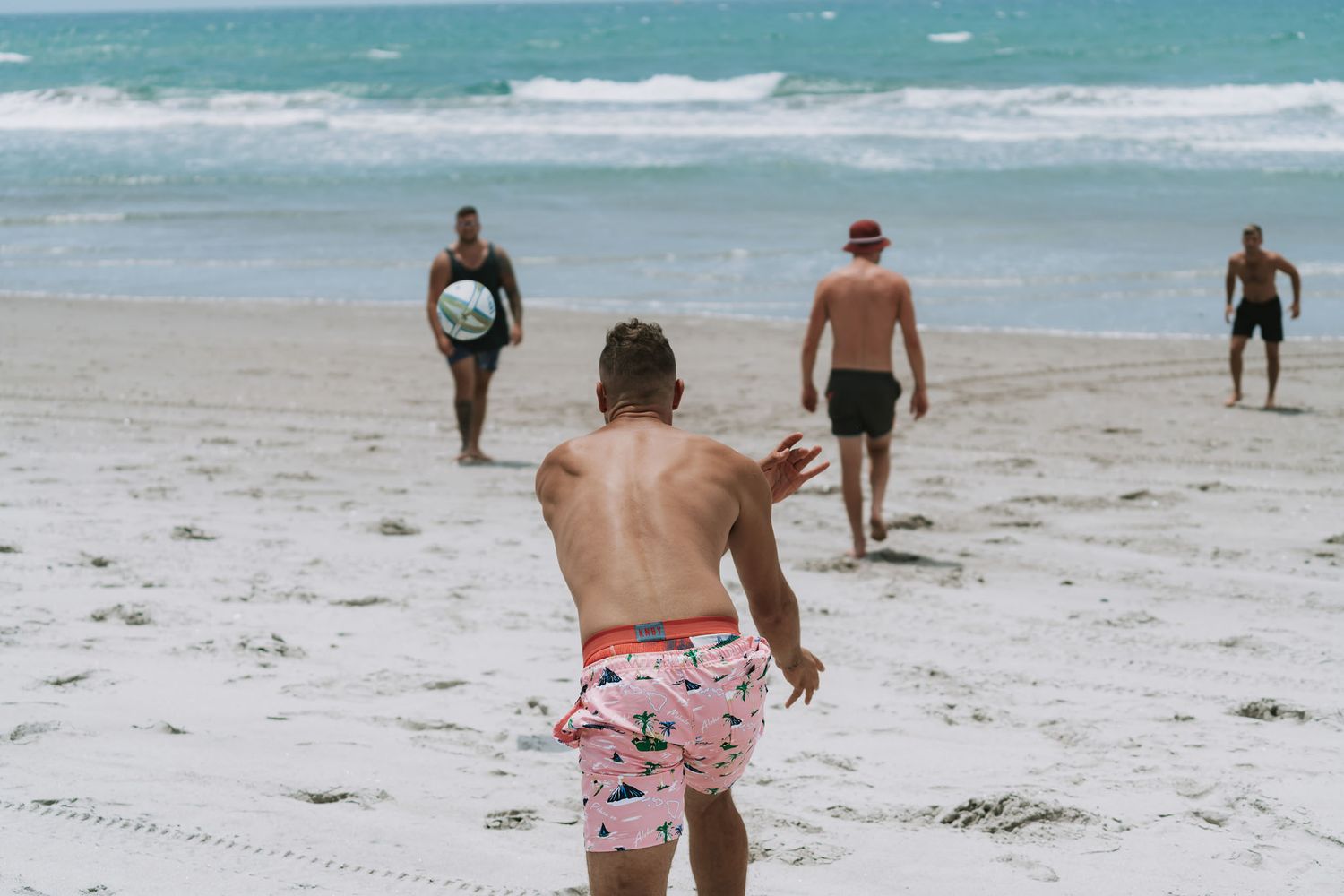 People walking and playing on a white sandy beach with turquoise ocean waves in the background on a sunny day.