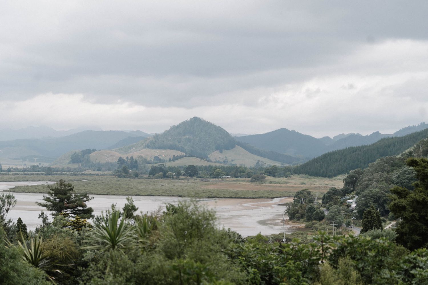 Panoramic aerial view of rugged mountains and misty valleys with scattered houses and roads in a rural landscape.