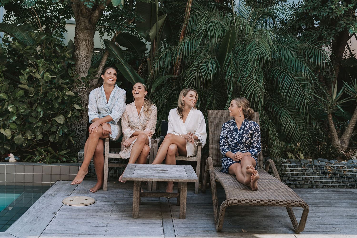 A group relaxes on lounge furniture by a pool surrounded by lush tropical palm trees and greenery.