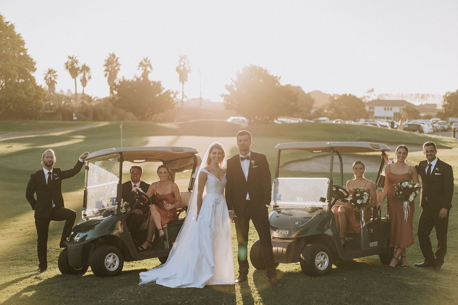 Wedding party posing with golf carts on a sun-drenched golf course during golden hour.
