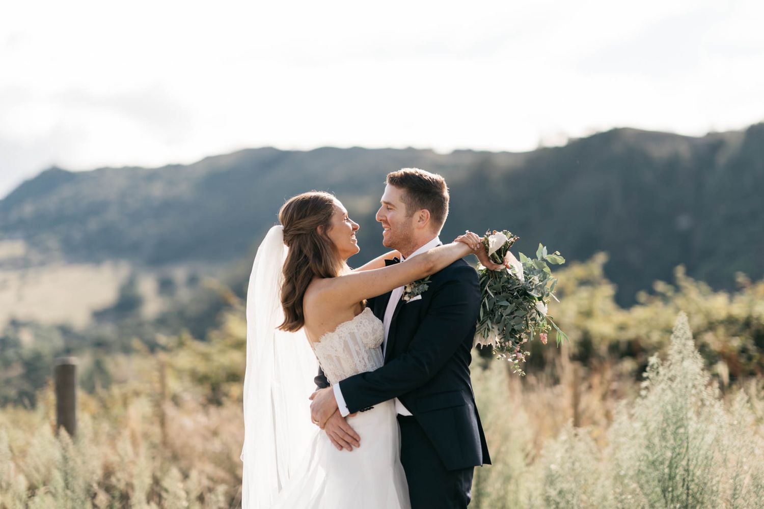 A couple embraces on their wedding day in front of scenic mountain landscape during golden hour.