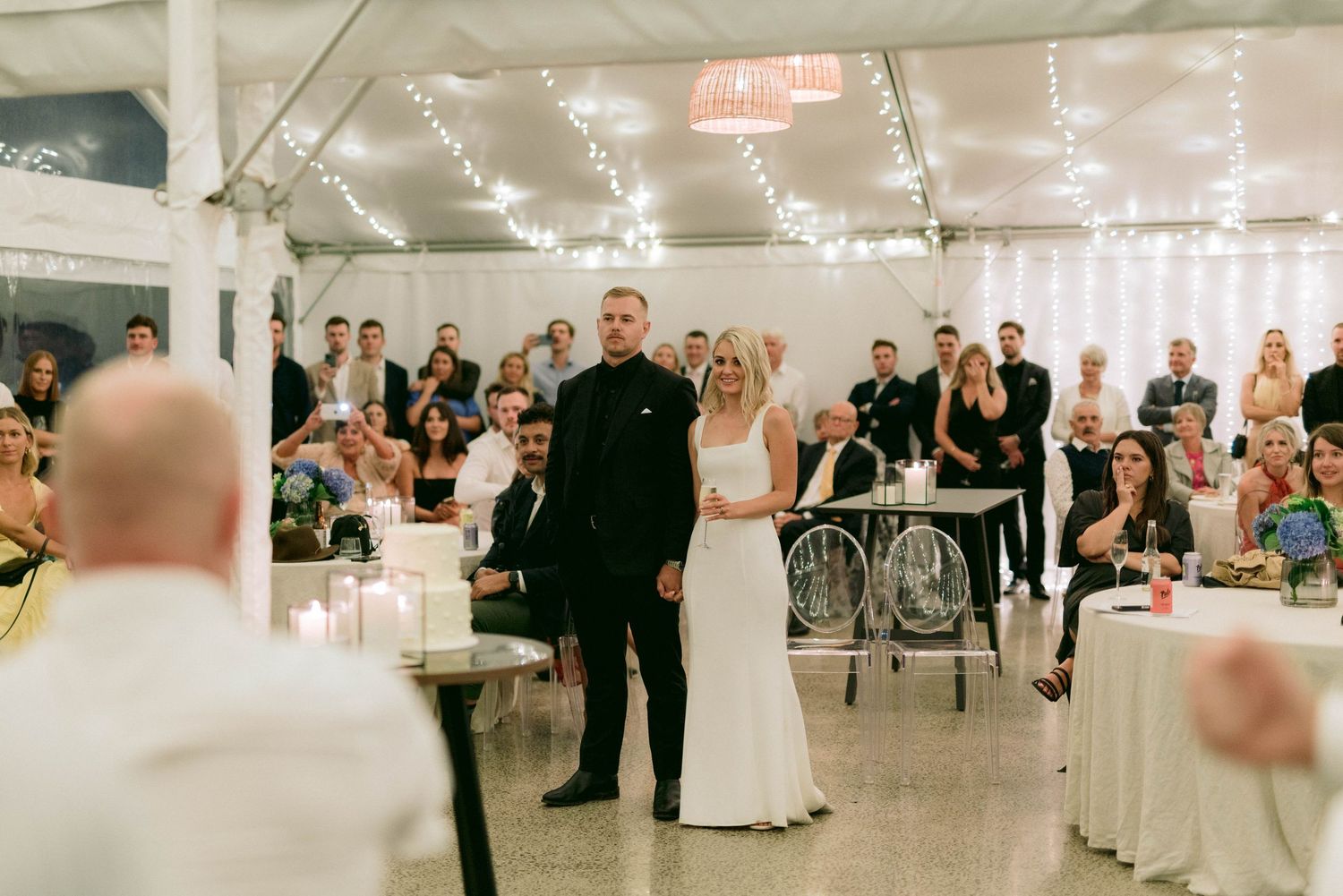 Wedding guests watch a couple during their reception in a decorated white tent.
