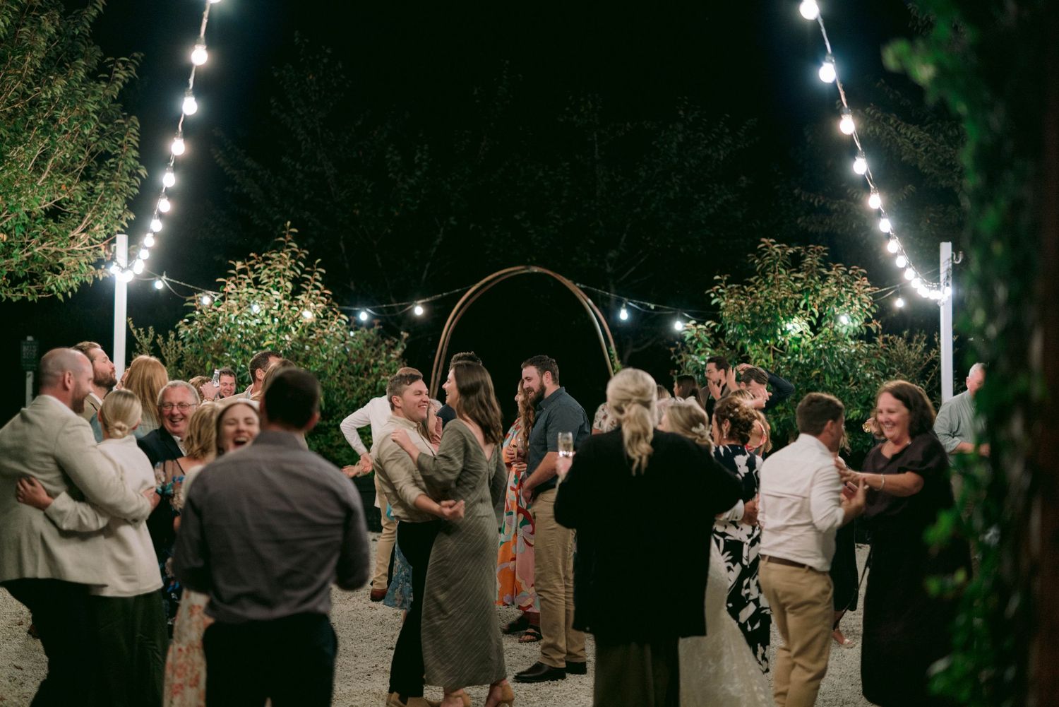 Evening outdoor wedding reception with string lights and guests dancing.