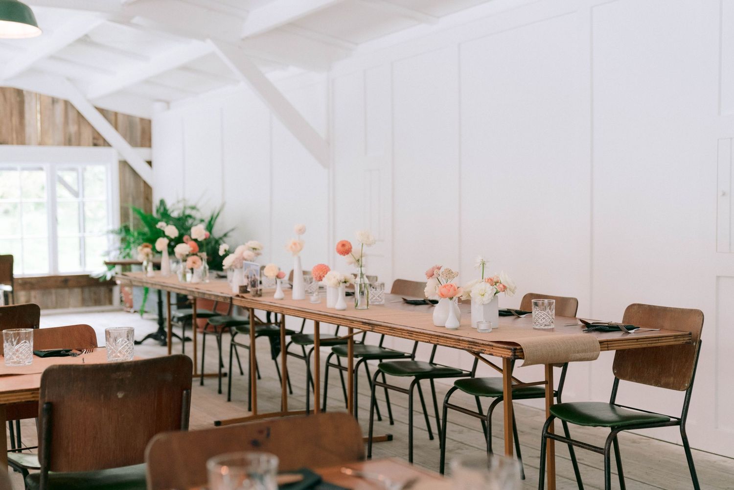 White rustic wedding reception venue with wooden tables decorated with floral centerpieces and vintage chairs.