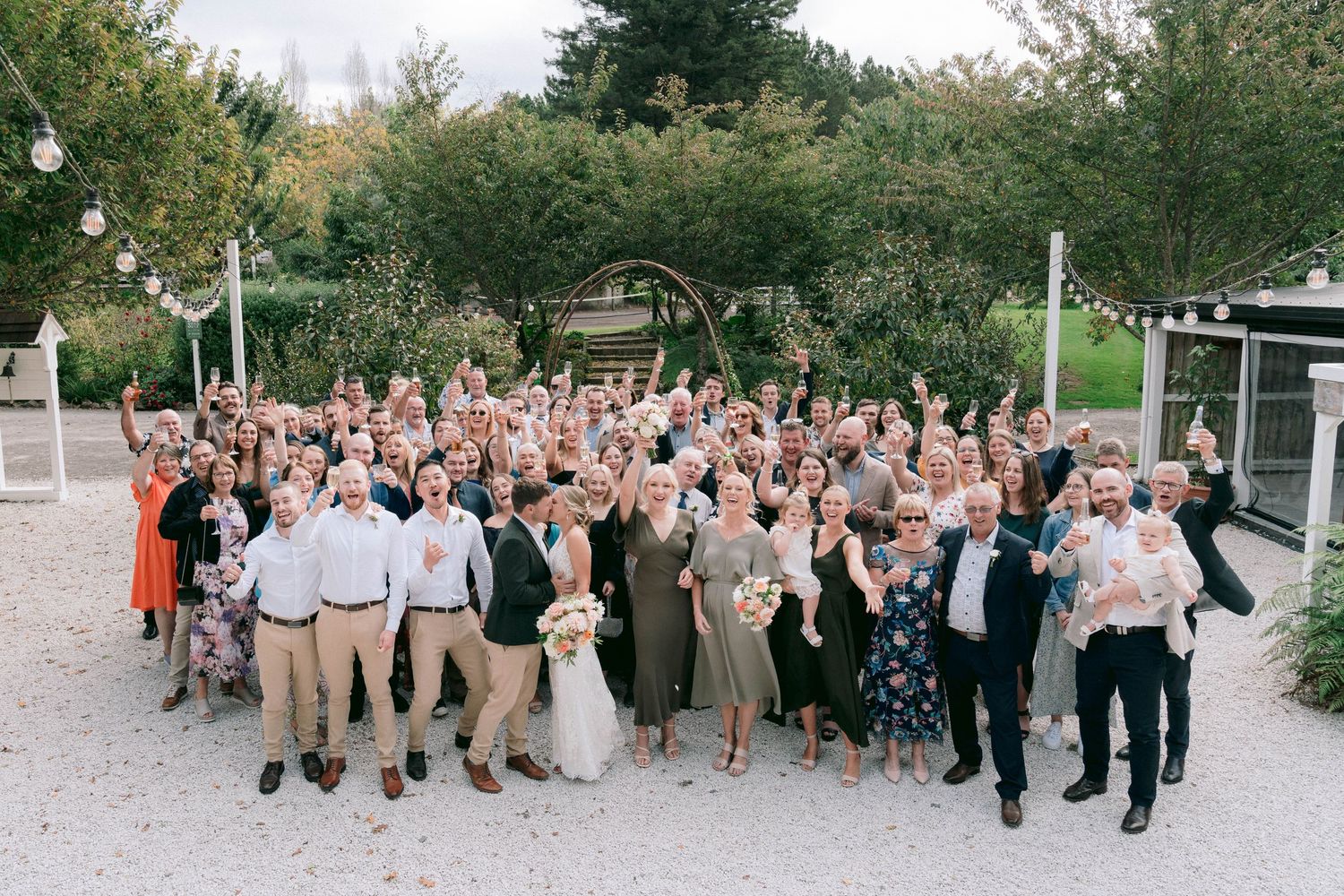 Large group of wedding guests walking together on a garden path during celebrations.