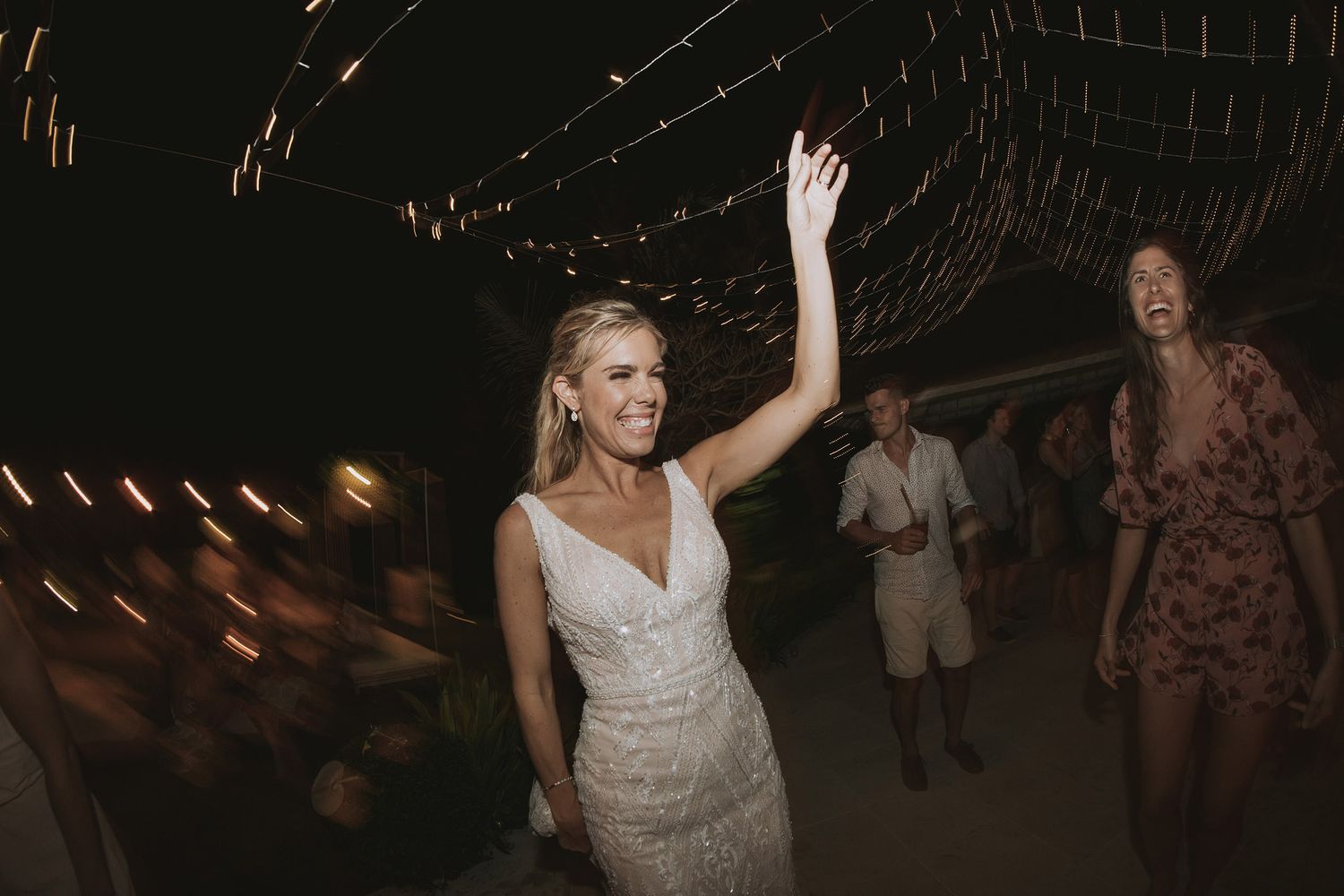 Wedding reception dance floor filled with guests dancing under dimly lit string lights.
