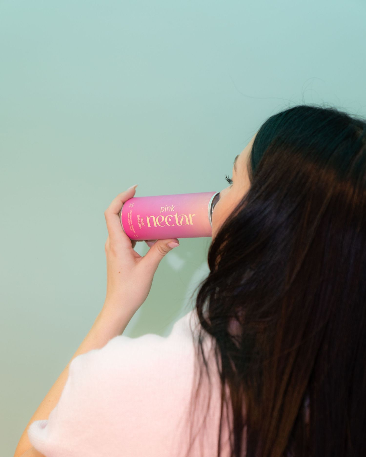A person drinking from a pink Nectar beverage can against a mint green background.