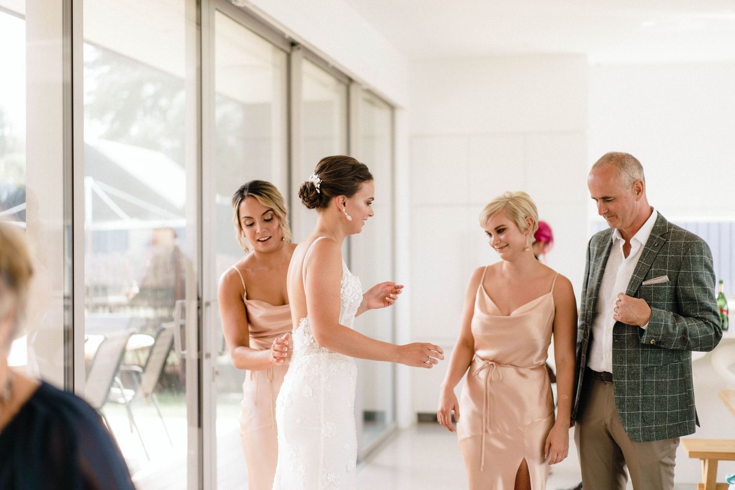 Wedding party in blush pink dresses gathered in modern hallway with natural light.