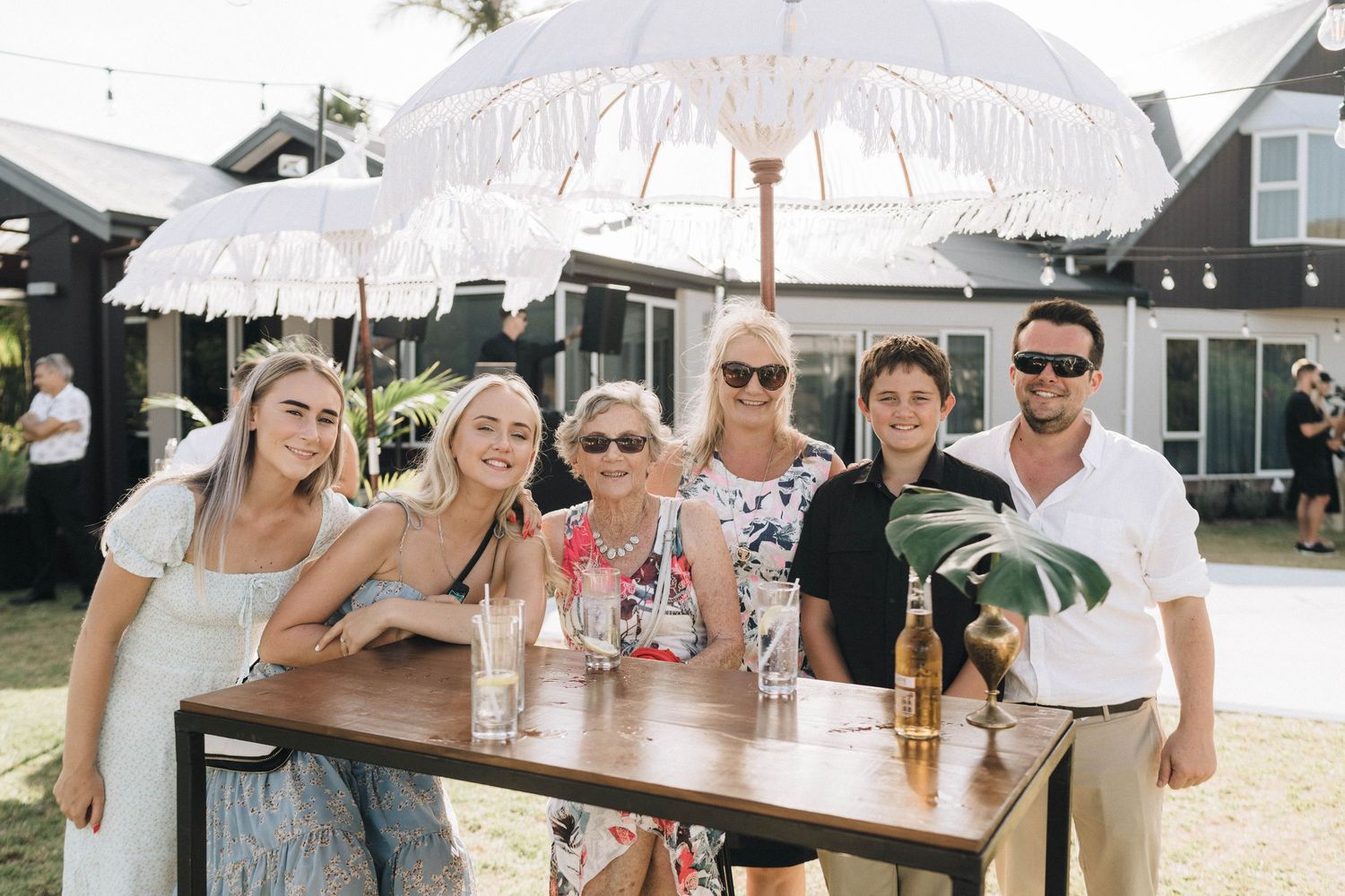Wedding guests enjoying drinks under white umbrellas at outdoor reception.