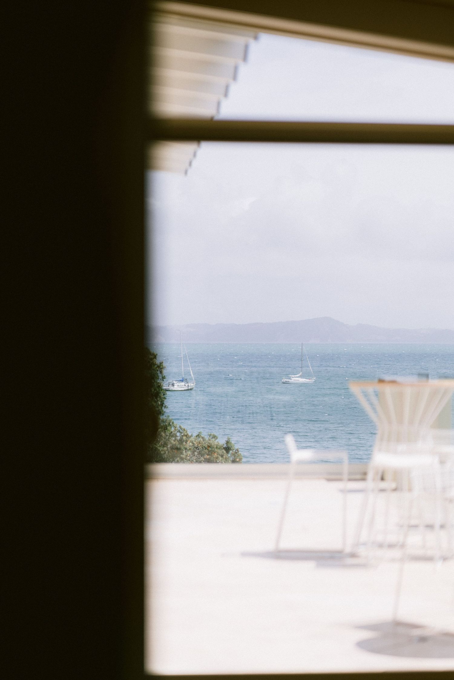 White chairs and tables arranged on a sunny oceanfront terrace with blue water views.