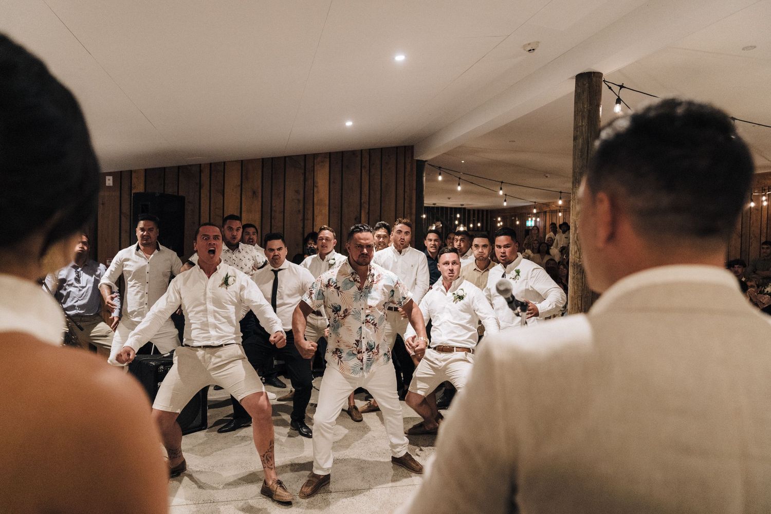 Wedding guests dancing and celebrating on wooden dance floor during indoor reception party.