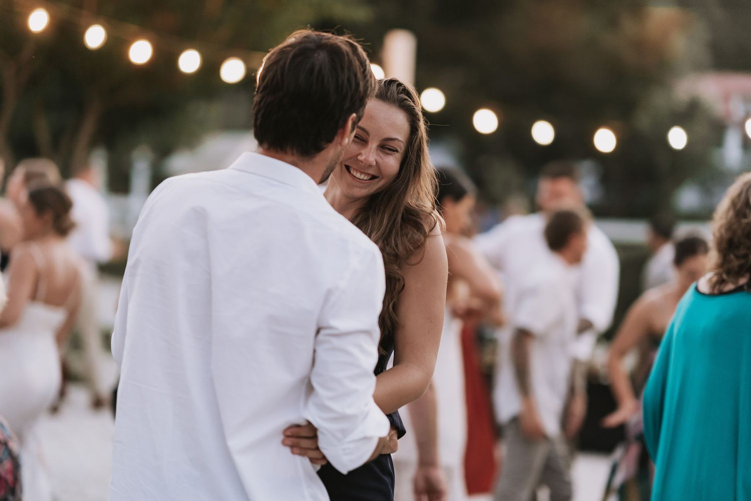 Guests dancing together on outdoor patio under warm string lights during evening wedding reception celebration.