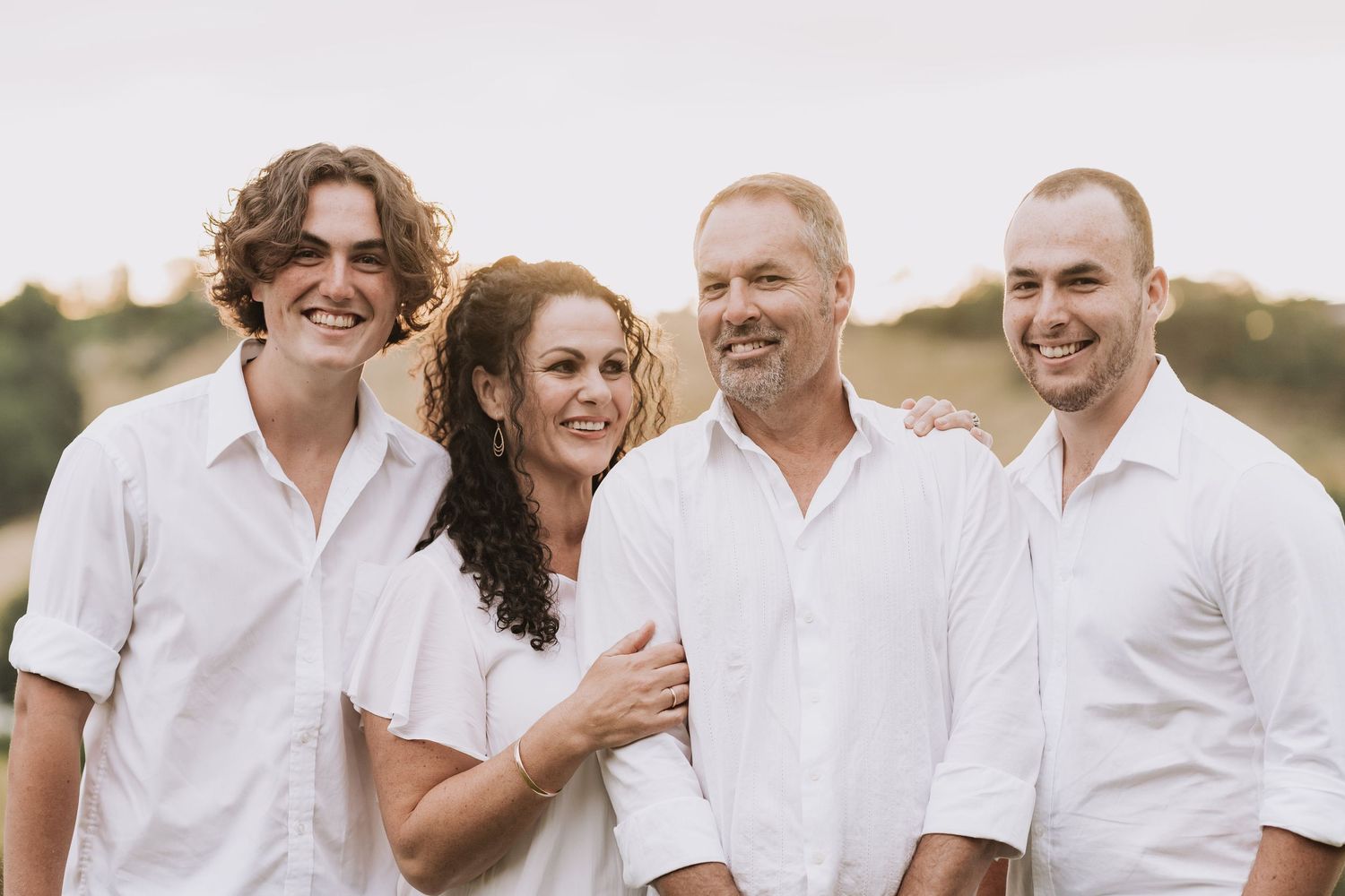 Group wearing white shirts and khaki pants laughs together outdoors during sunset photoshoot.