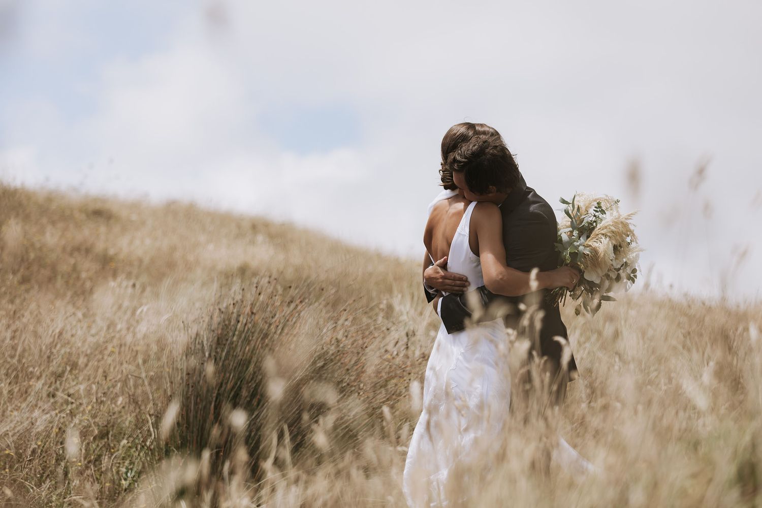 A person walks through tall golden grass on a hillside during a warm sunset hour.