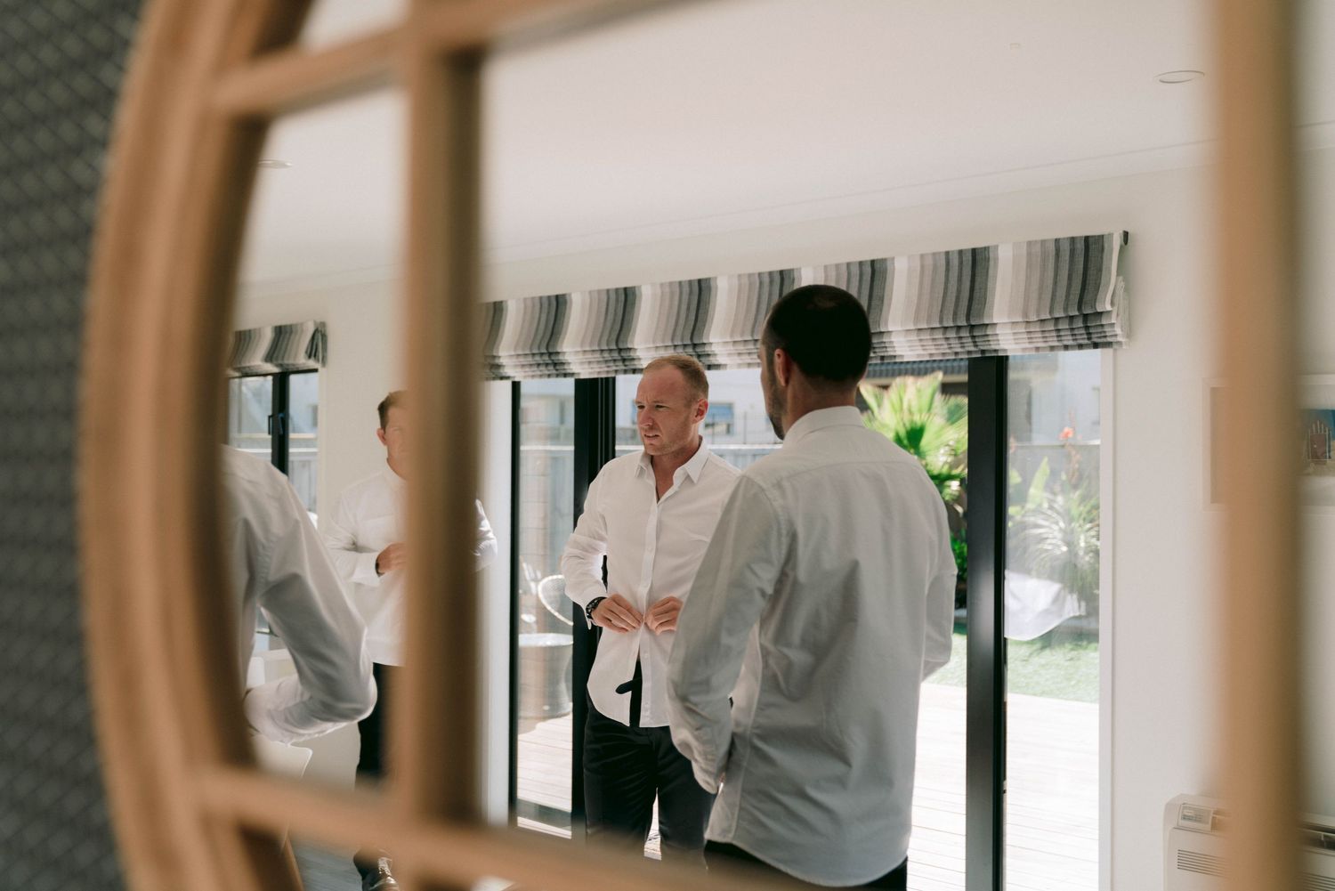 A reflection in a circular mirror shows people in white shirts having a conversation in a bright interior space.