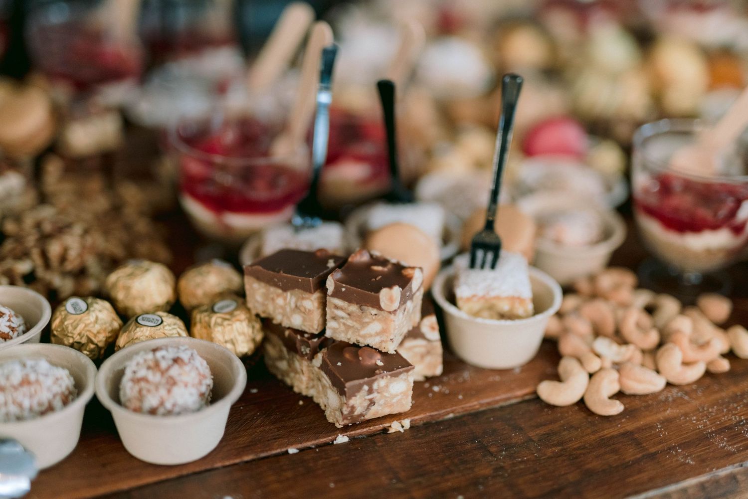 Various elegant desserts and treats displayed on a rustic wooden table at a wedding reception.