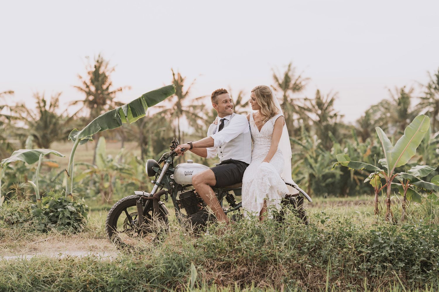 A couple enjoying a romantic moment in a lush tropical garden with palm trees and greenery in soft natural lighting.