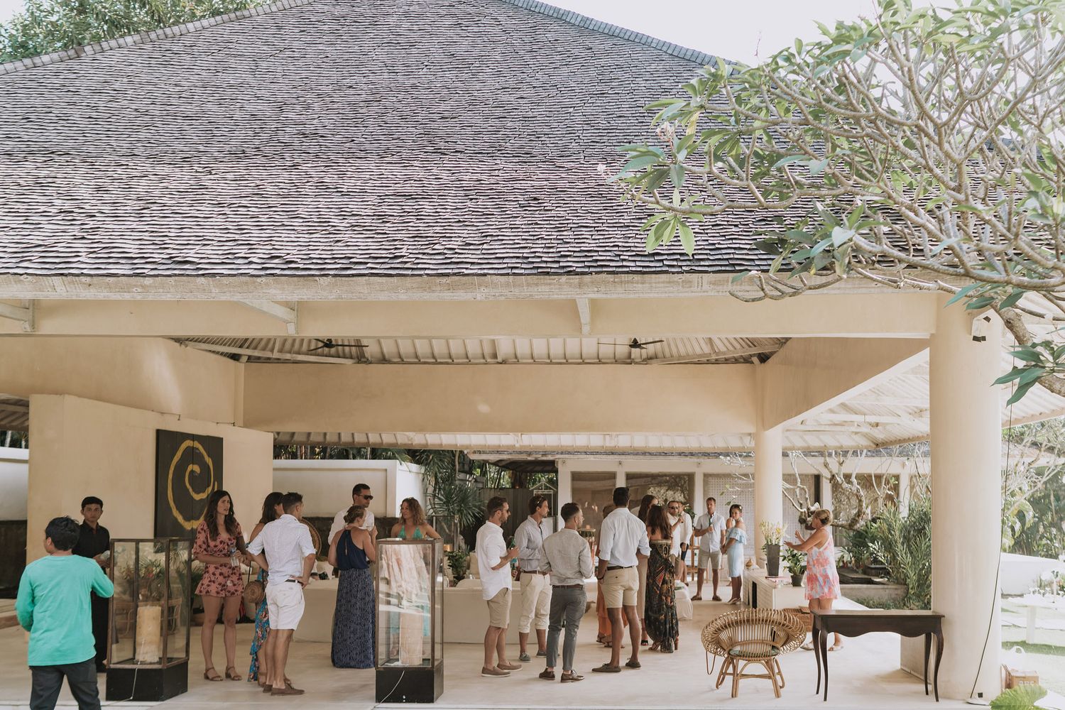 People gathering under an elegant covered outdoor pavilion area with natural decor and seating arrangements.