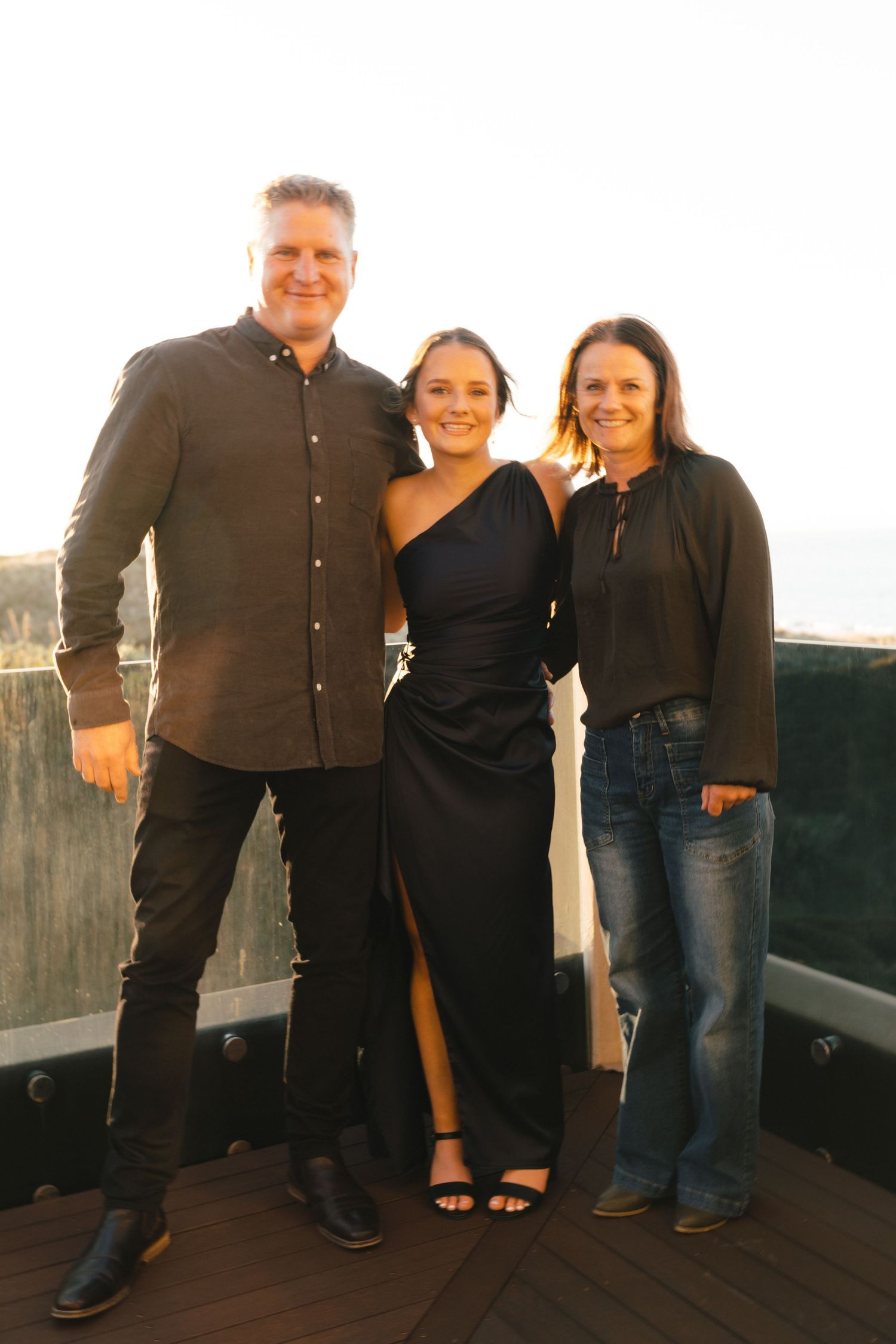 A group poses together on a wooden deck at sunset with mountains in the background.