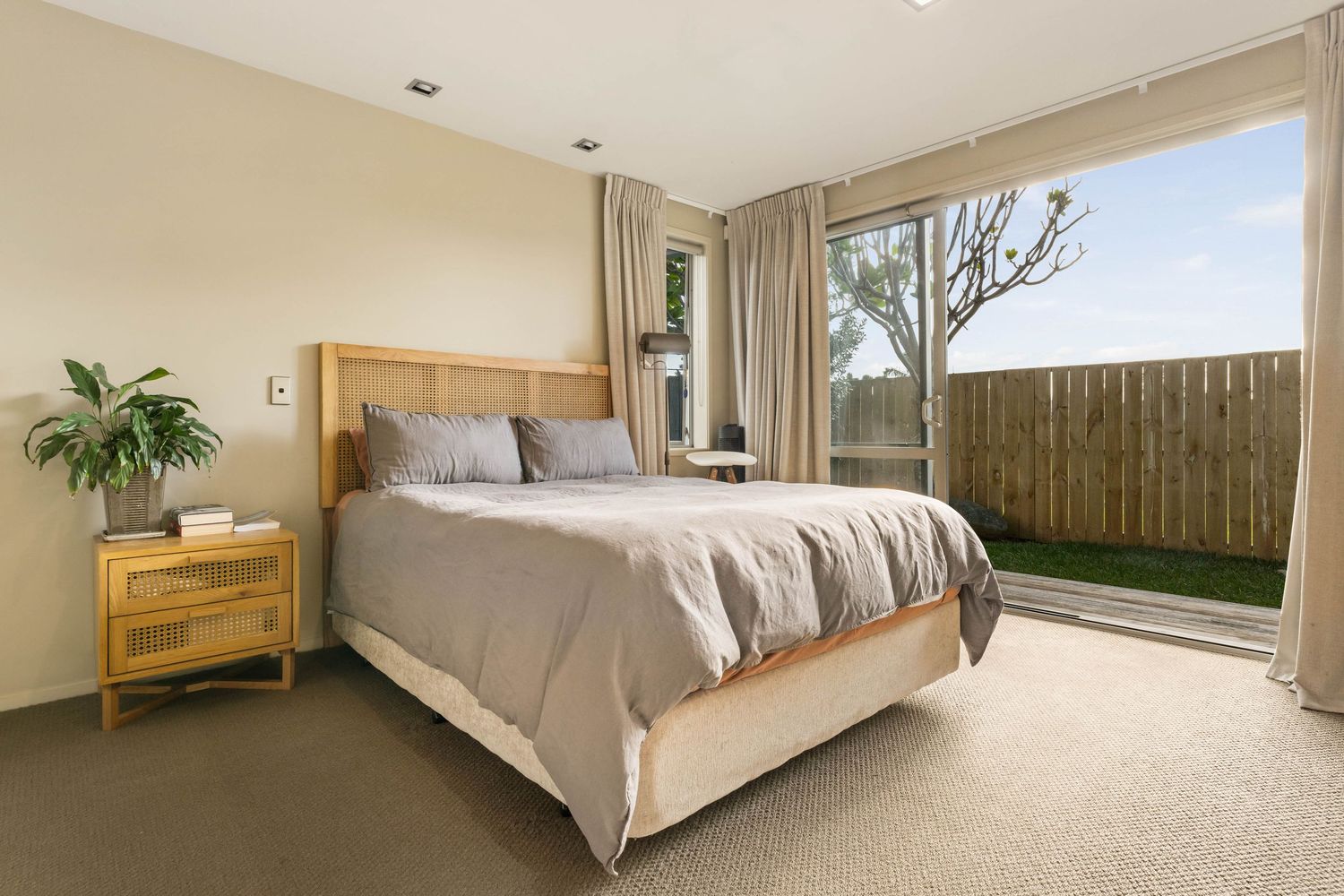 Contemporary bedroom with beige tones featuring a plush bed and natural lighting from wide windows.