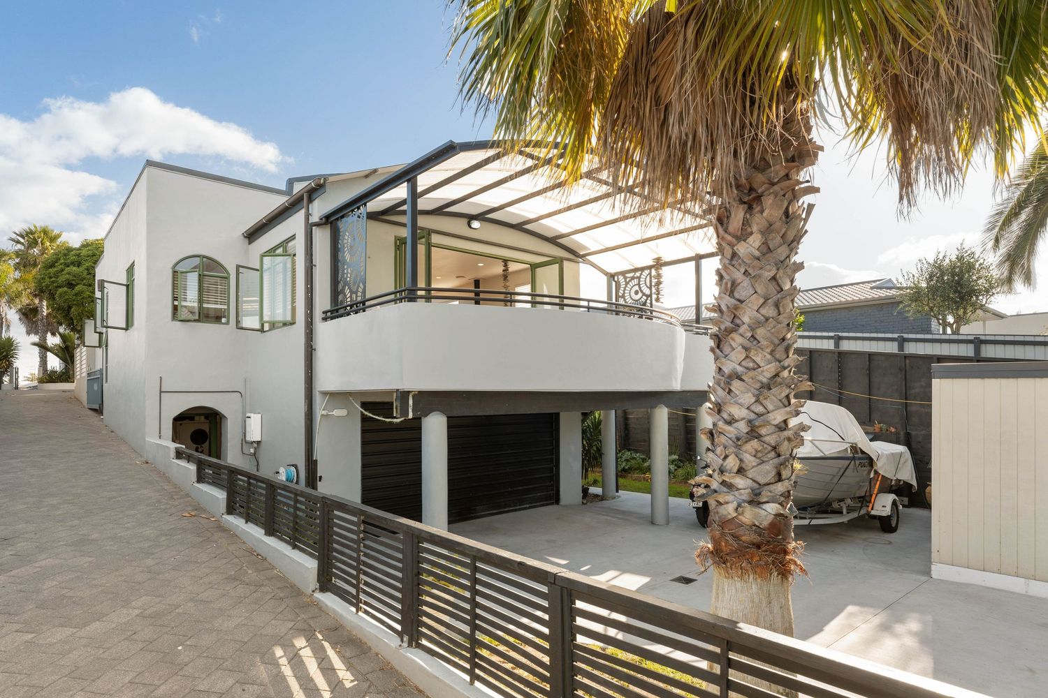 Contemporary white coastal home with glass balcony, covered outdoor space and palm tree landscaping.