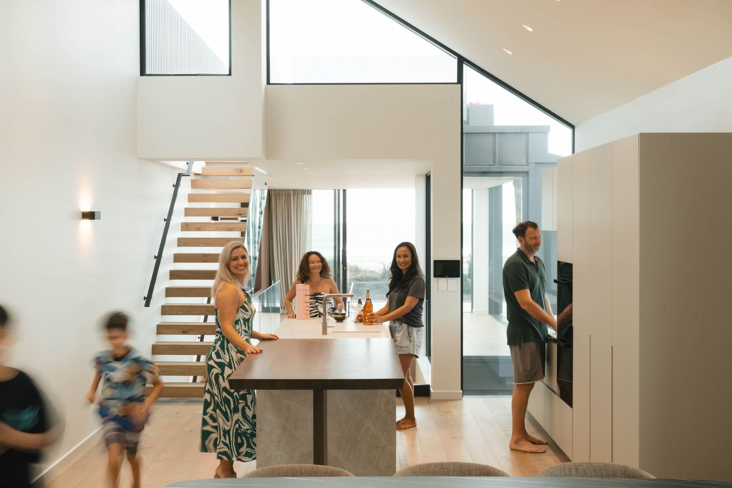 Modern open concept kitchen with high ceilings and natural light shows a group gathering at a white dining table.