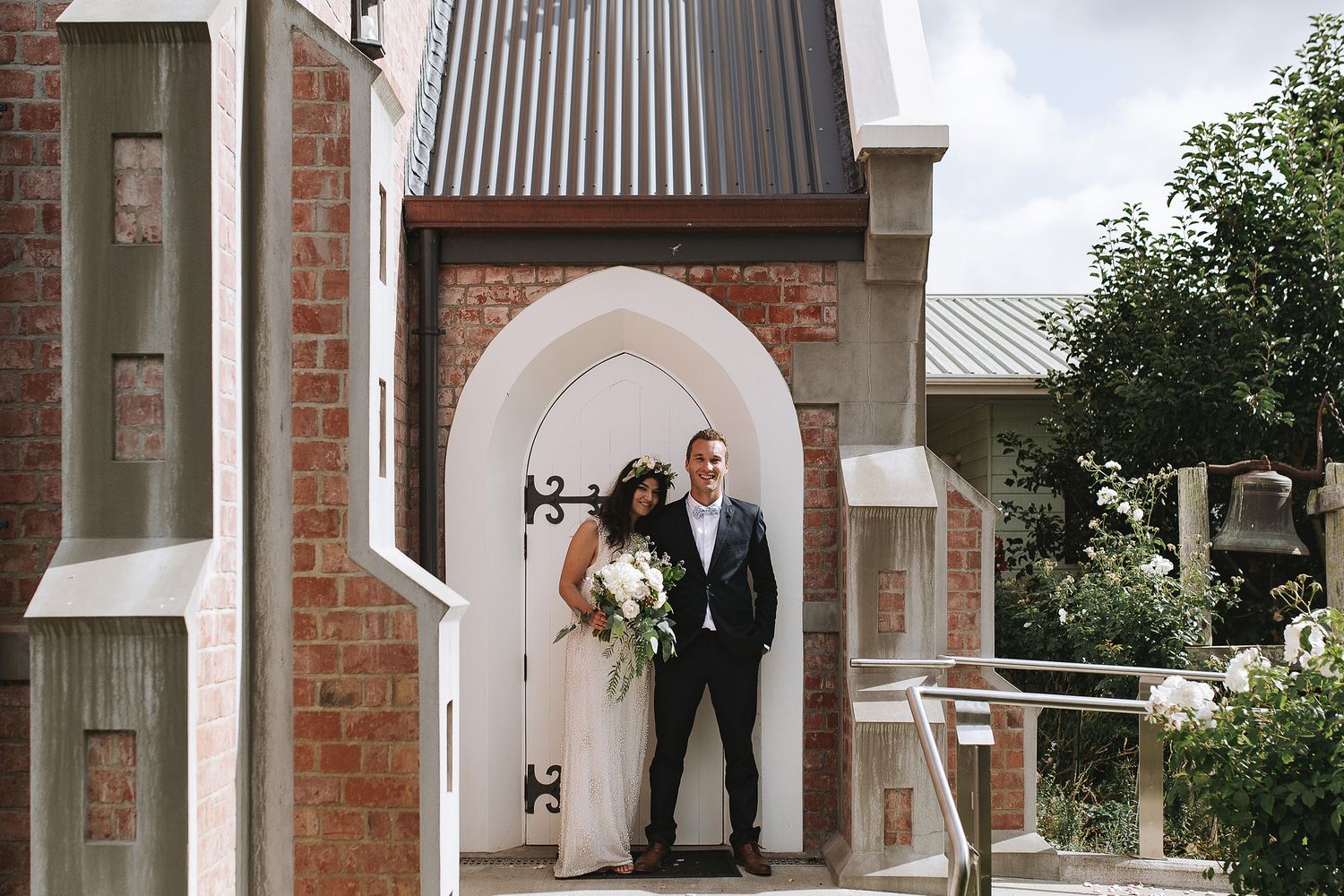A newlywed couple stands beneath an elegant arched brick entryway during a garden wedding ceremony.