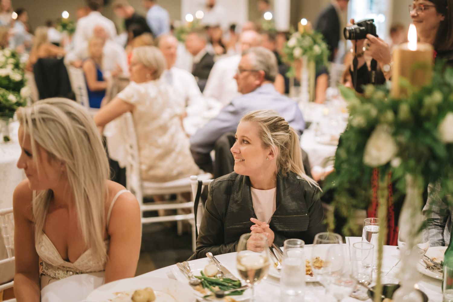 A candid shot of guests at an elegant wedding reception with white floral centerpieces and formal table settings.