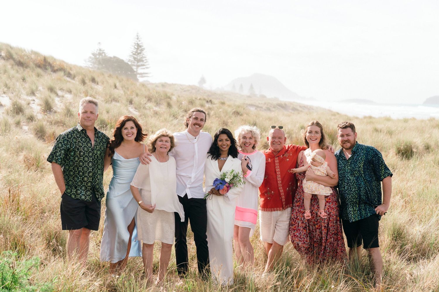 Wedding group portrait of family and friends on scenic hillside overlooking the ocean.