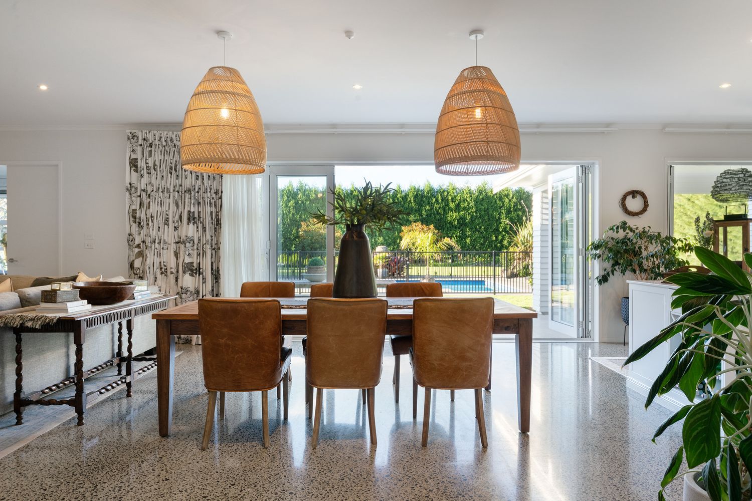 Open plan dining space with wicker pendant lights and large glass doors leading to outdoor area.