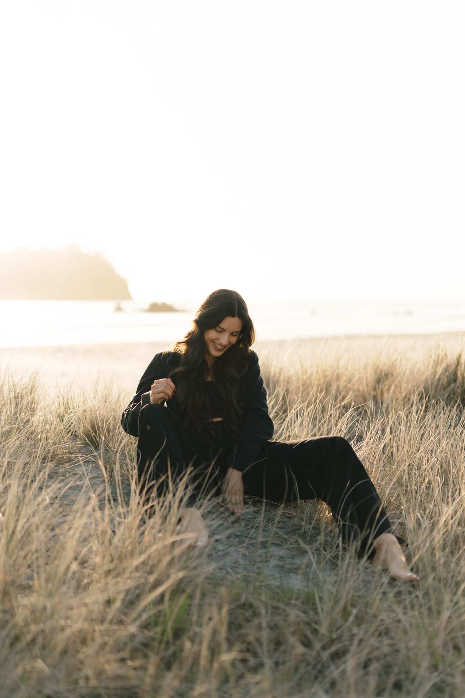Figure in dark clothing poses gracefully in tall golden grass at sunset.
