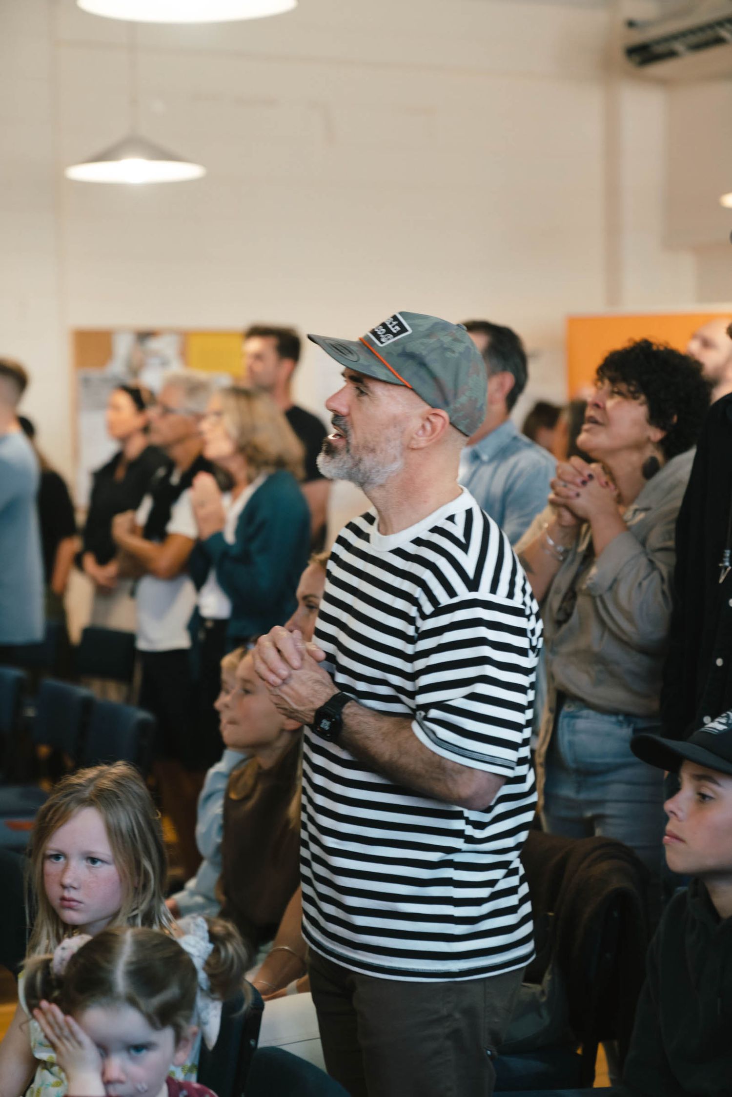 Audience members standing and watching a performance, including someone in a striped shirt.