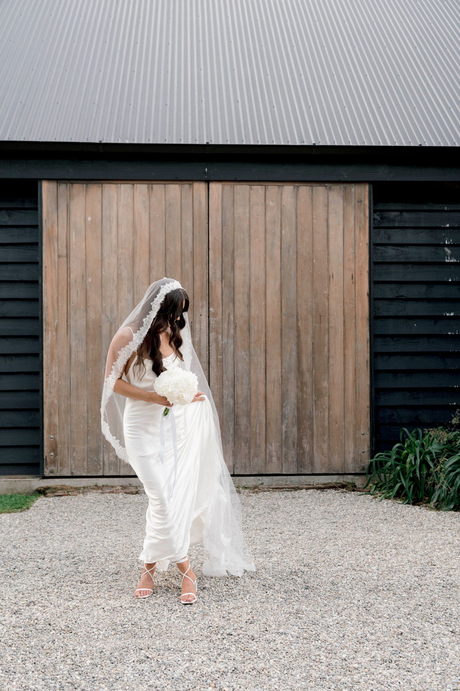 A white bridal gown flowing in the wind against a rustic wooden barn wall.