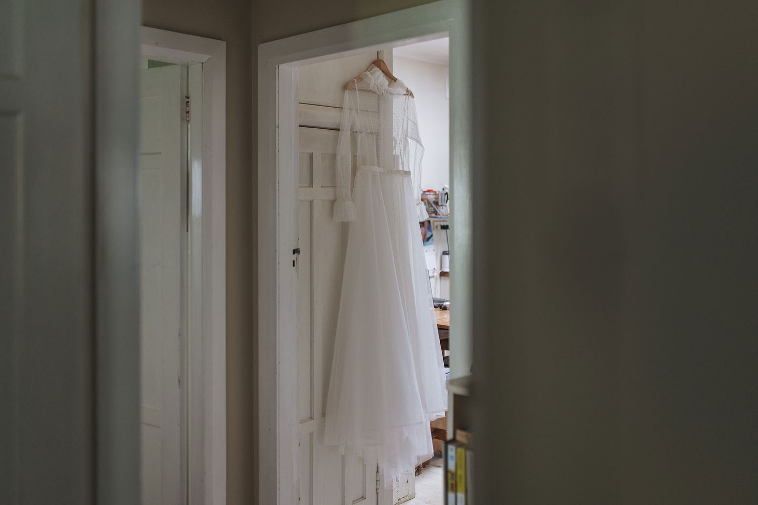 Sleeveless ivory wedding dress hangs elegantly on a white padded hanger in a brightly lit room.