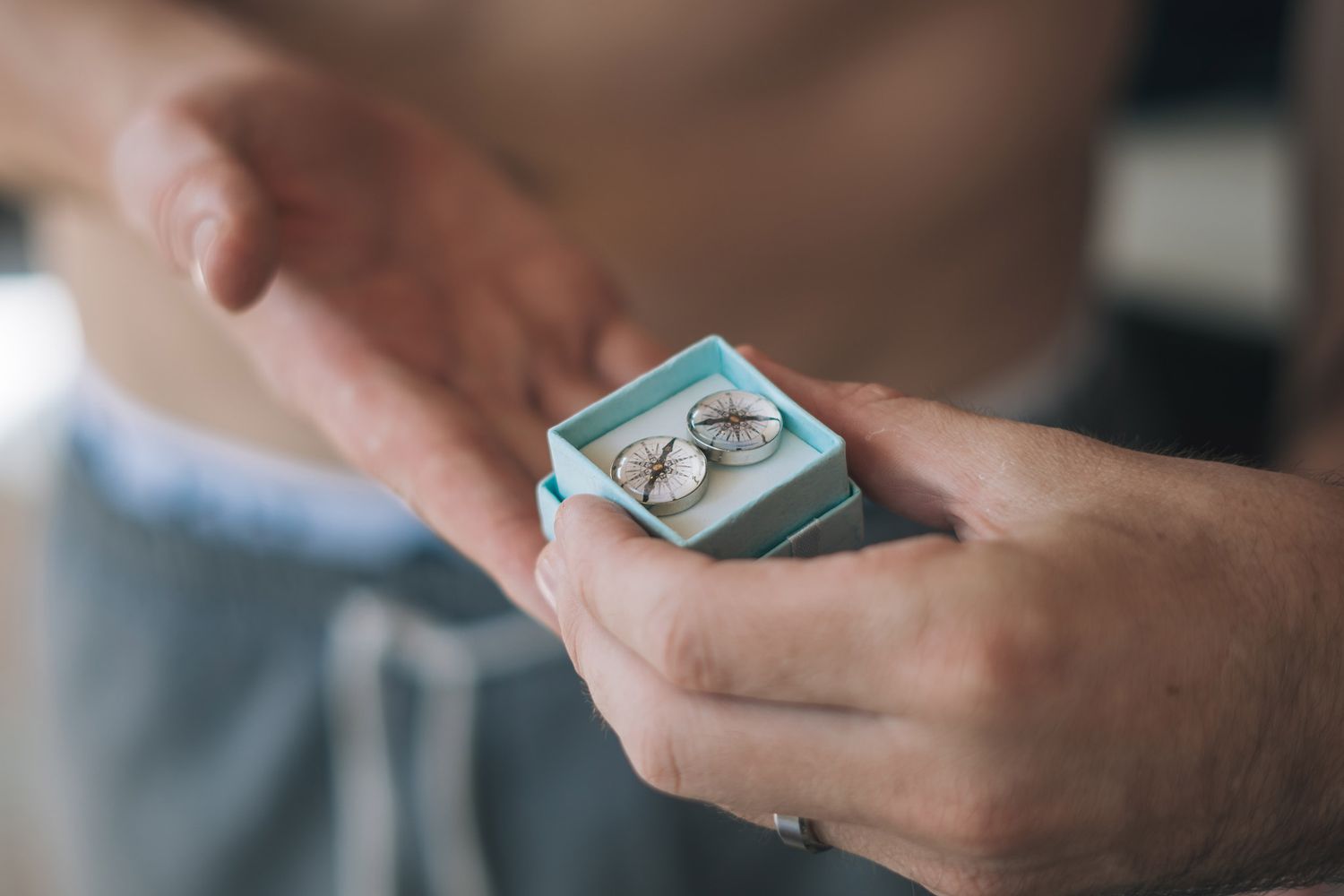 Close-up view of hands holding a small teal ring box with engagement ring inside.