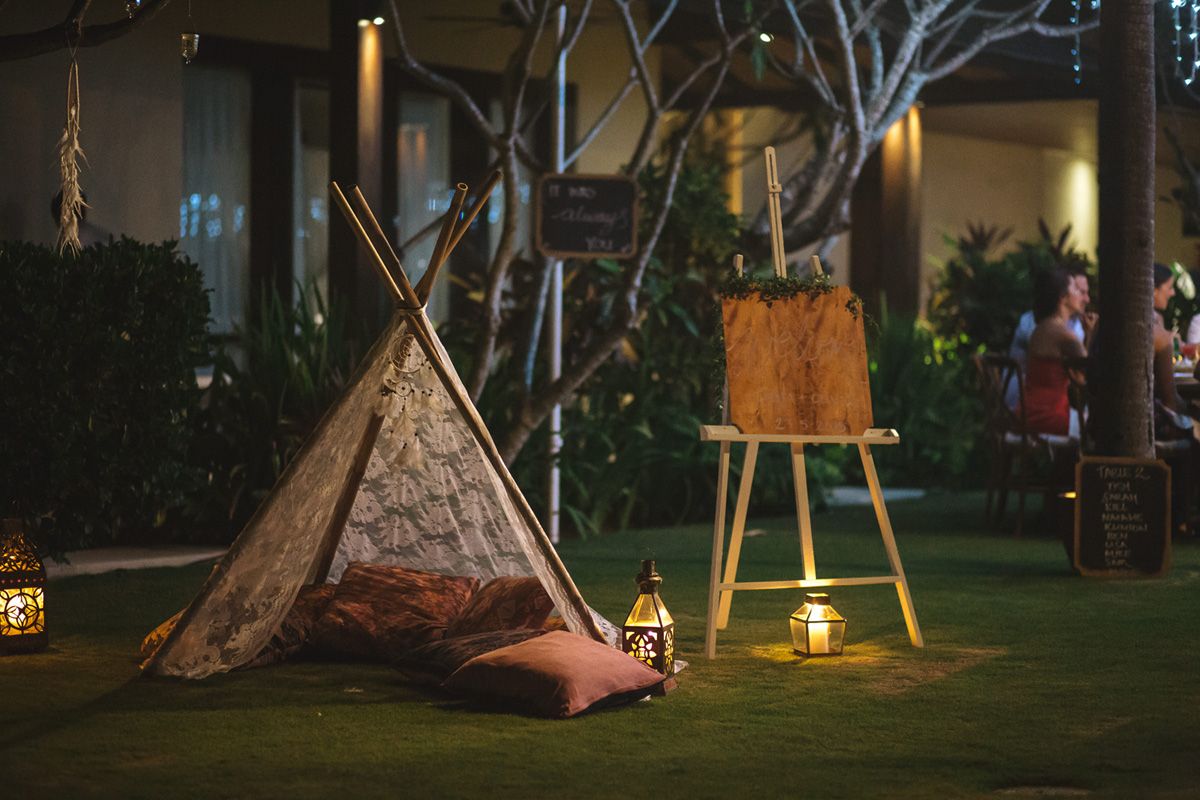 Outdoor evening wedding venue setup with teepee structures and string lights.
