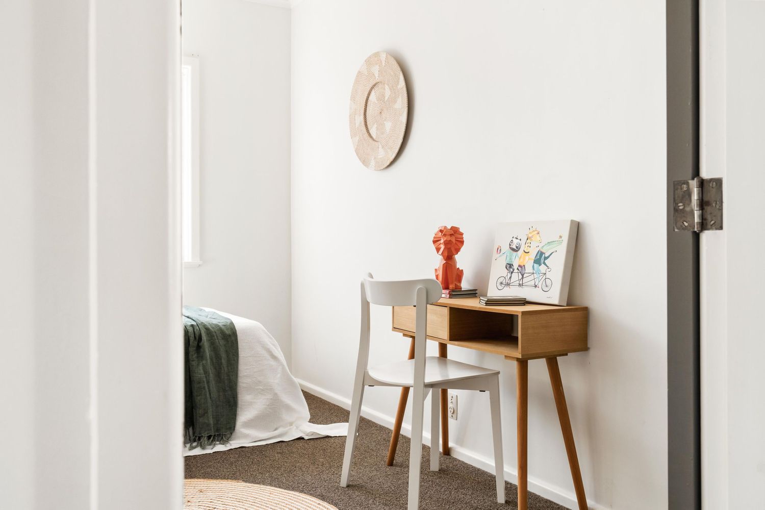Minimalist bedroom corner featuring a wooden desk, chair and decorative wall clock.